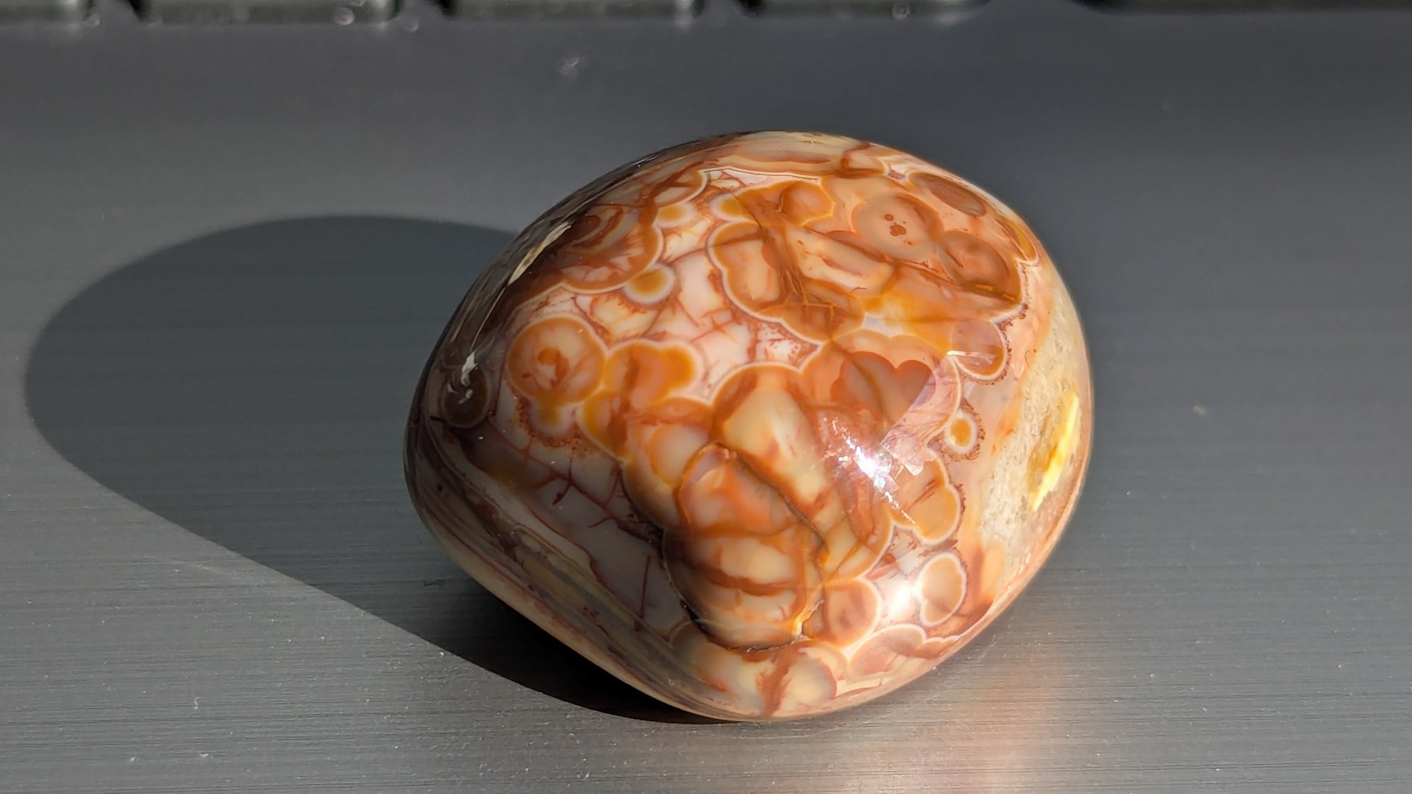 Rounded tumbled stone with a web of orange veins, photographed in direct sunlight