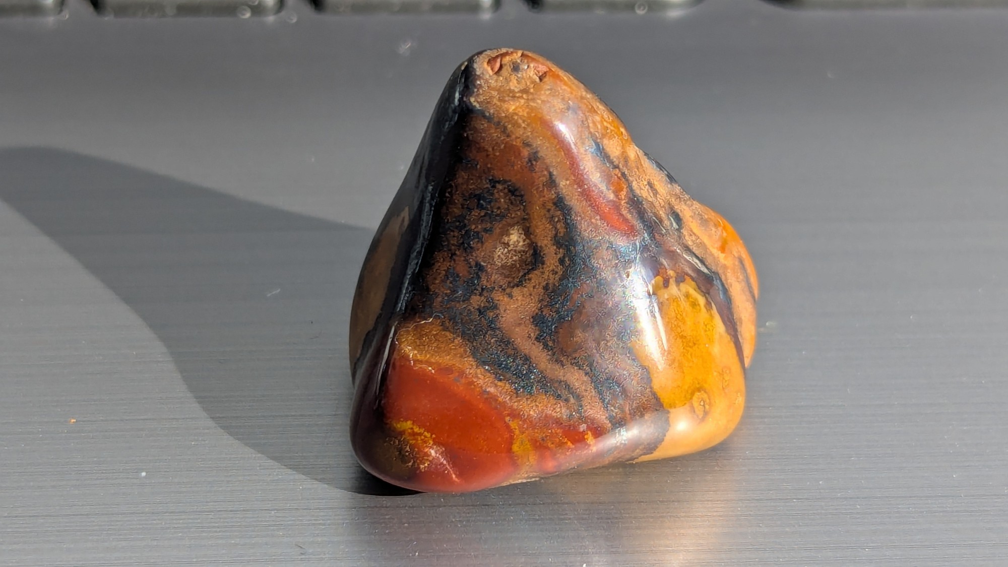 Small tumbled stone in black, rust and mustard standing upright, photographed in direct sunlight