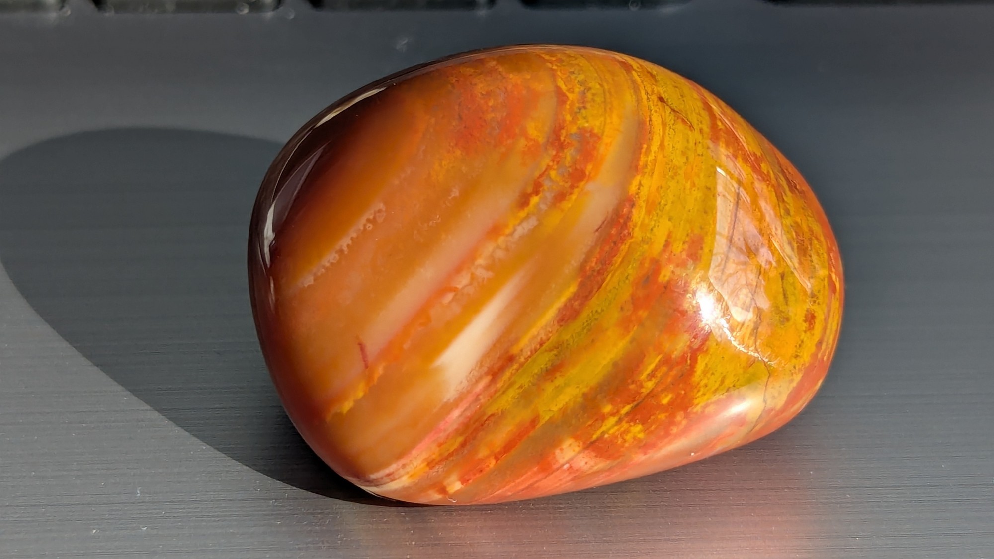 Tumbled stone in orange with streaks of yellow, photographed in direct sunlight