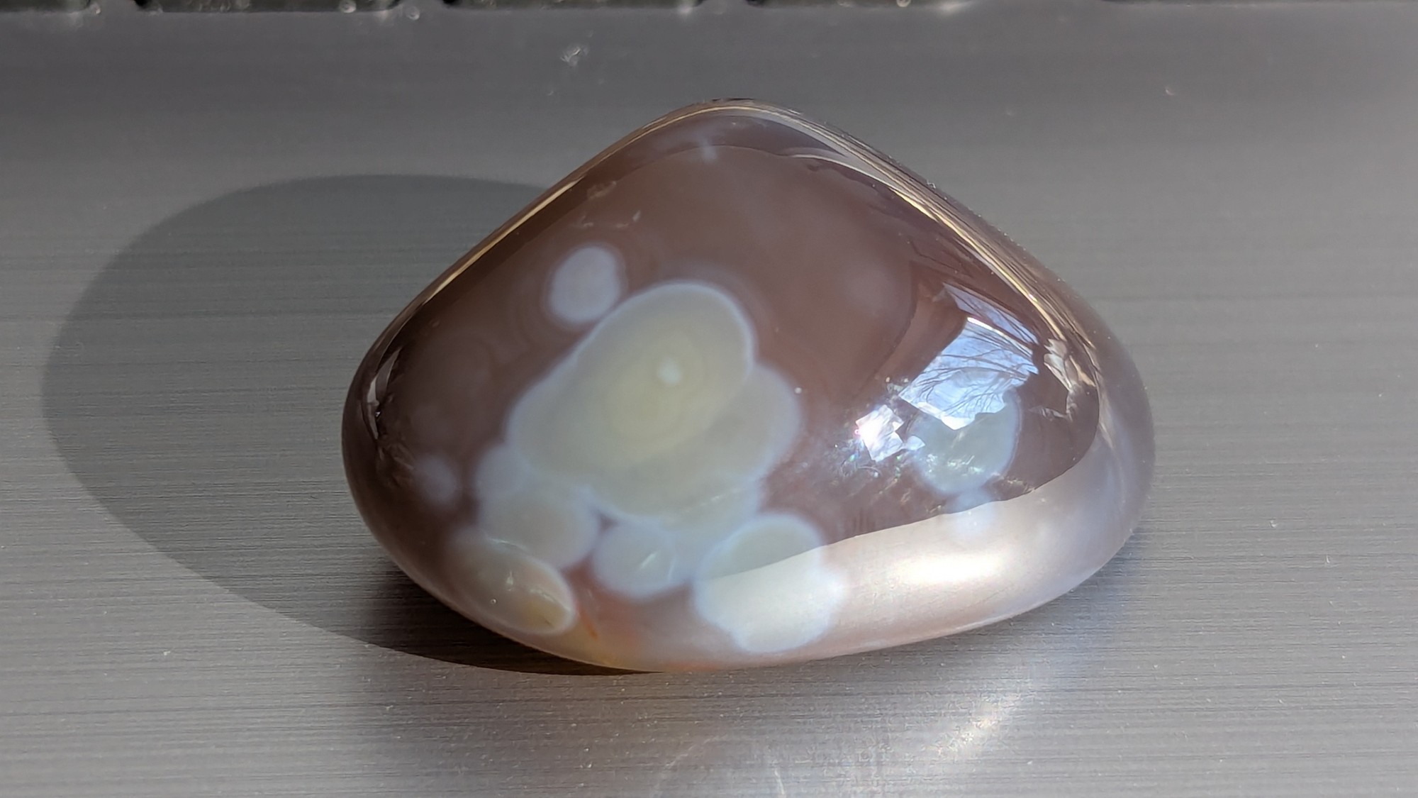 Brown tumbled stone with pale green and white orbs, photographed in direct sunlight