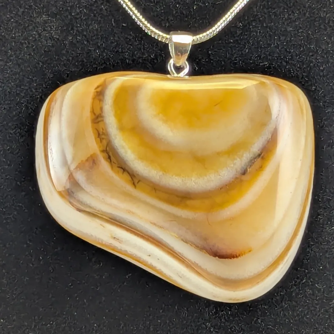 Rounded honey-colored agate pendant with curved cream and tan bands and fine dark threads along one band, on a silver-tone bail and snake chain, against a black background