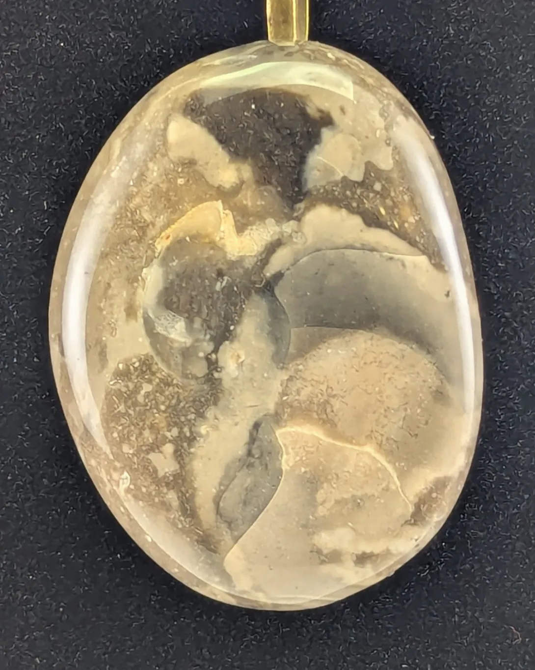 Large oval chert pendant with drifting patches of dark gray, cream and tan, on an antique bronze-tone bail and chain, against a black background