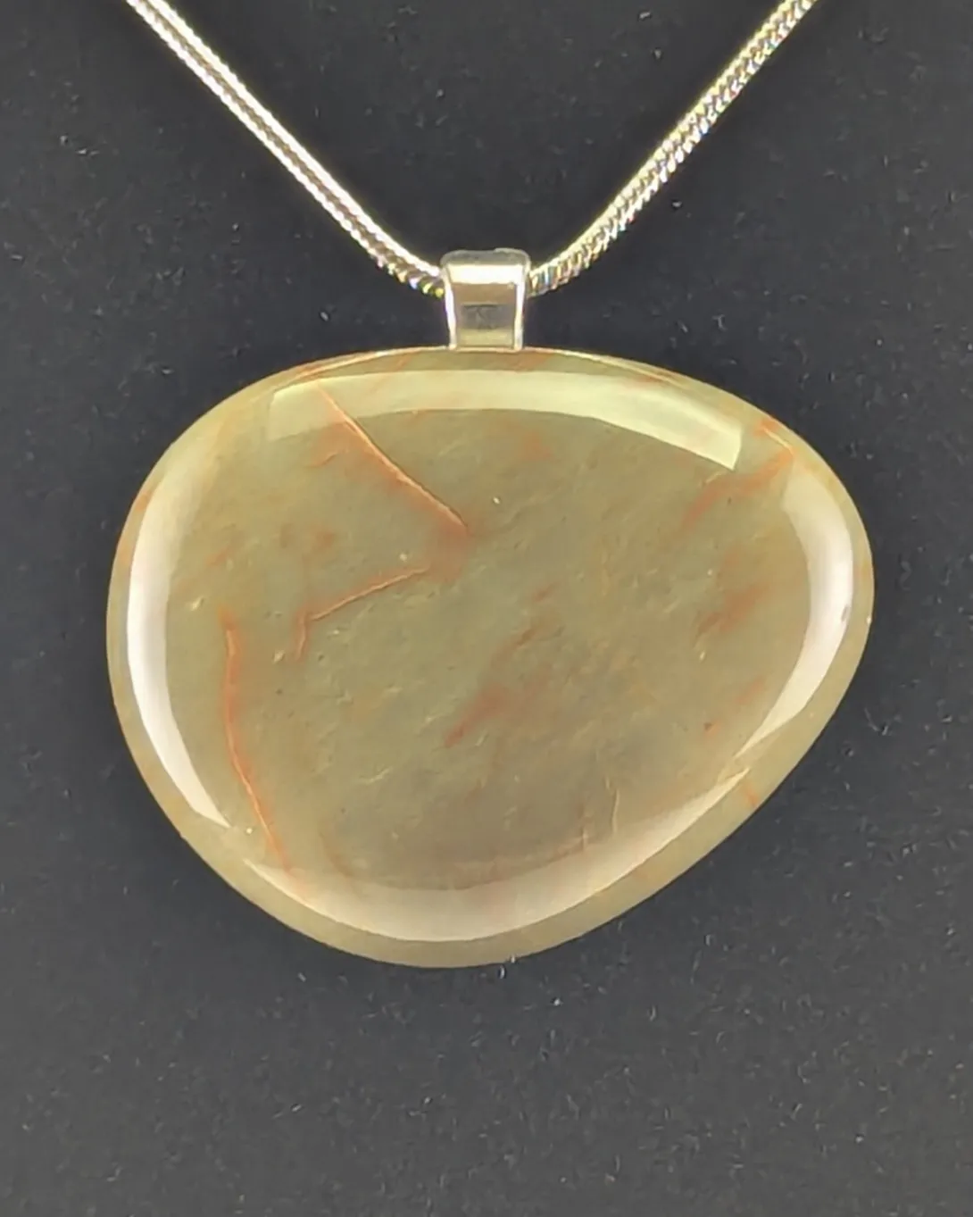 Rounded tan-green bloodstone pendant with thin rust-red veins, on a silver-tone bail and silver snake chain, against a black background