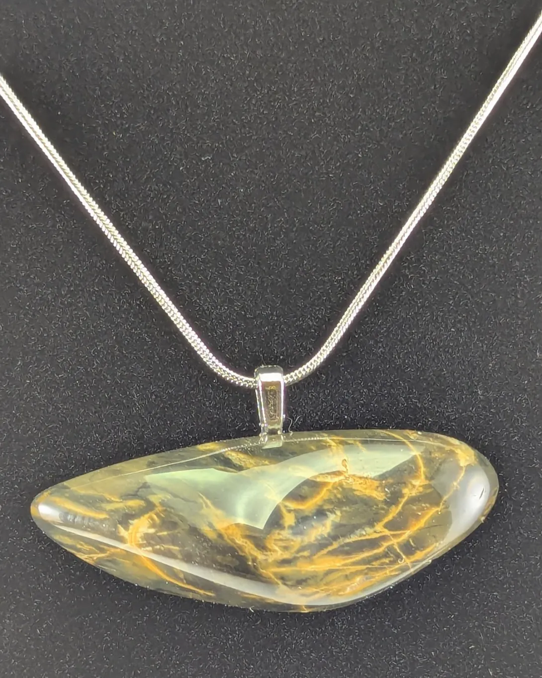 Long, narrow green jasper pendant with a web of golden yellow lines running through it, hanging horizontally from a silver-tone bail and snake chain, against a black background