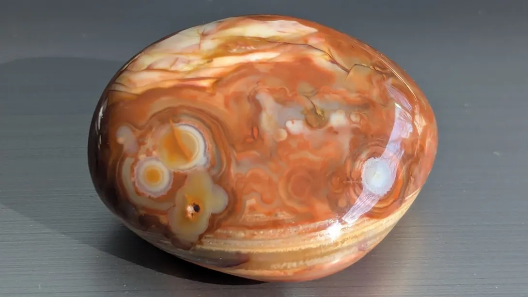 Rust and orange tumbled stone with bullseye swirls, photographed in direct sunlight