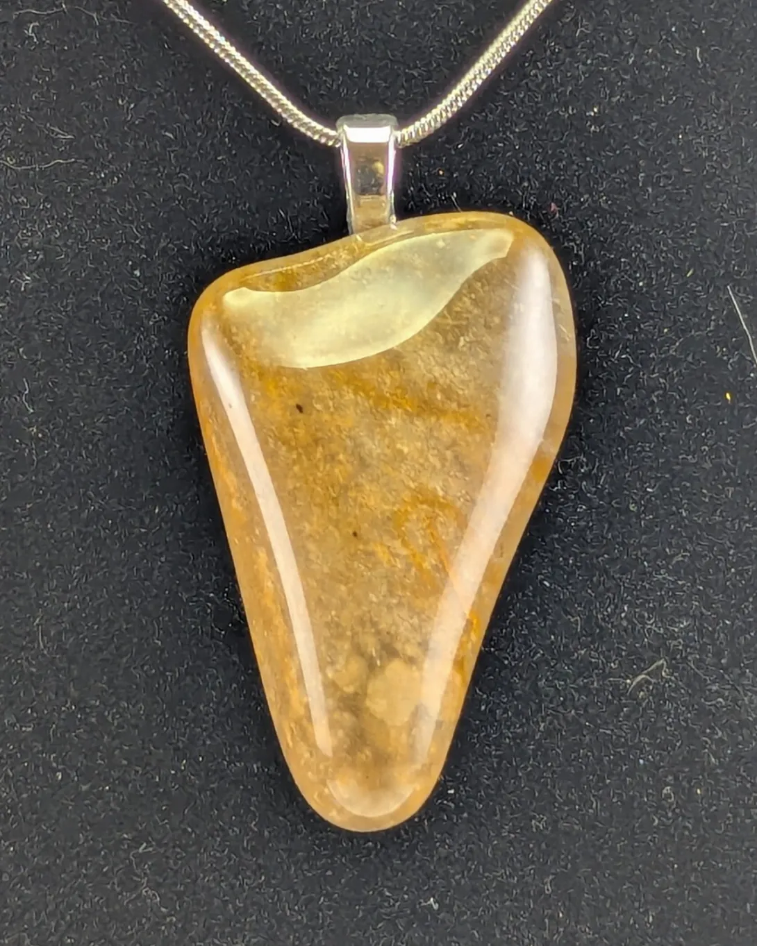 Triangular polished chert pendant in honey and rust tones, on a silver bail and chain against black velvet
